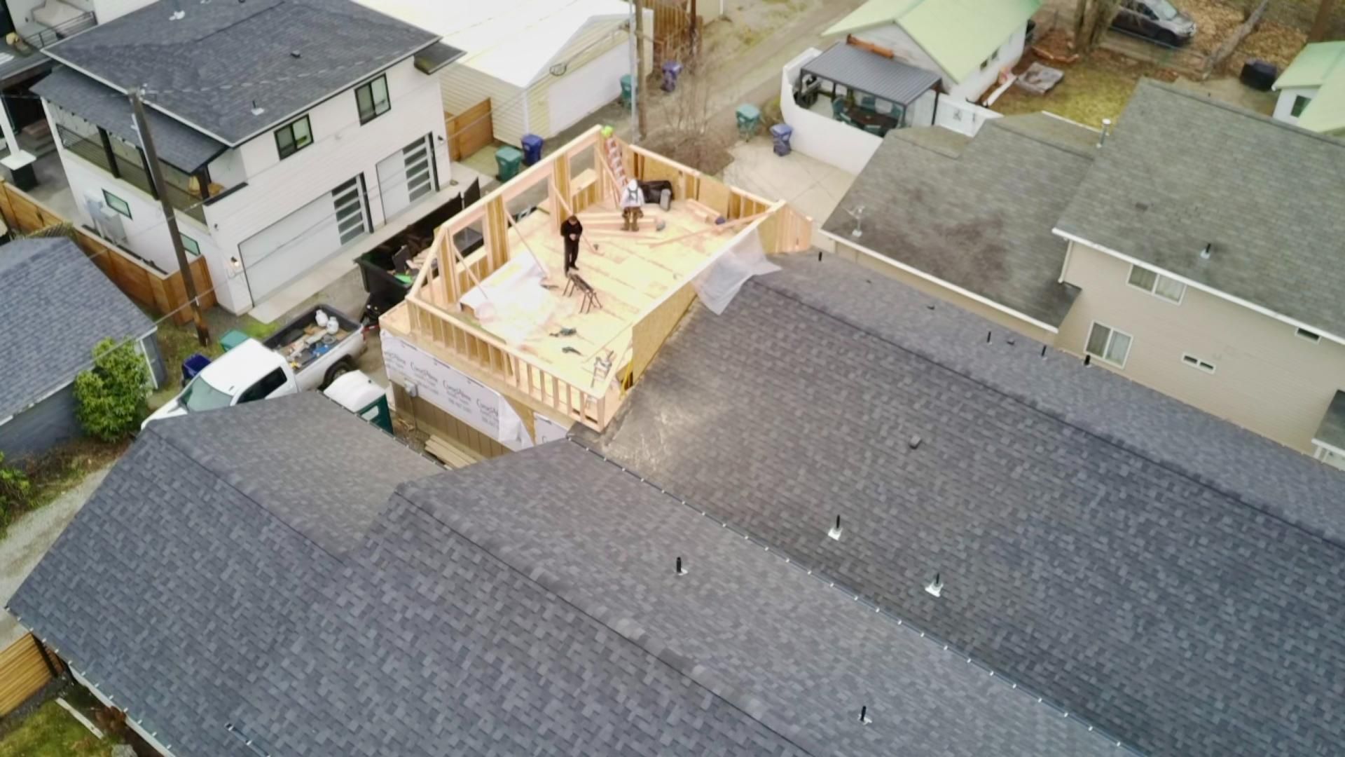 Construction of a second-story addition on a house, viewed from above. Carpenter working on the wooden frame.