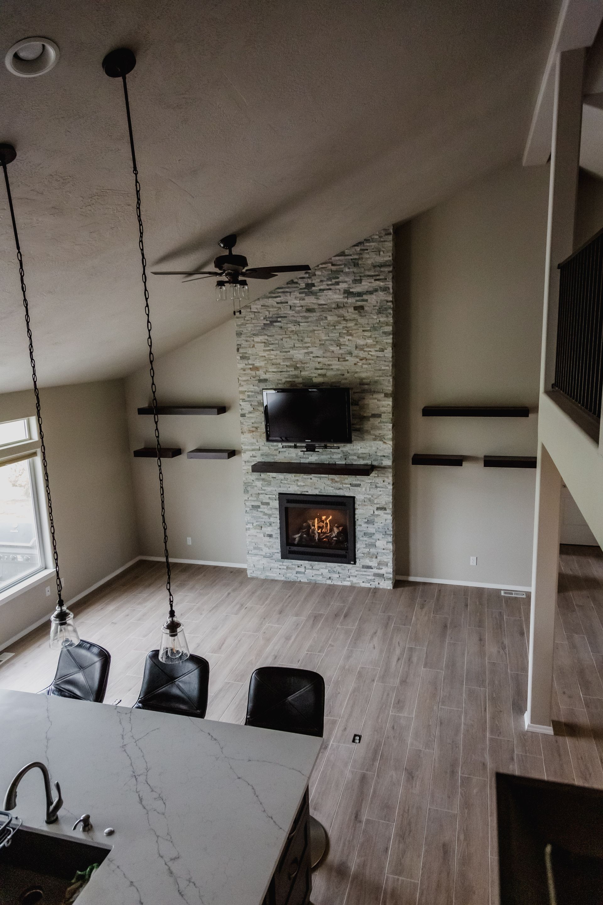 Modern living room with fireplace, TV, stone accent wall, and kitchen island with pendant lights.