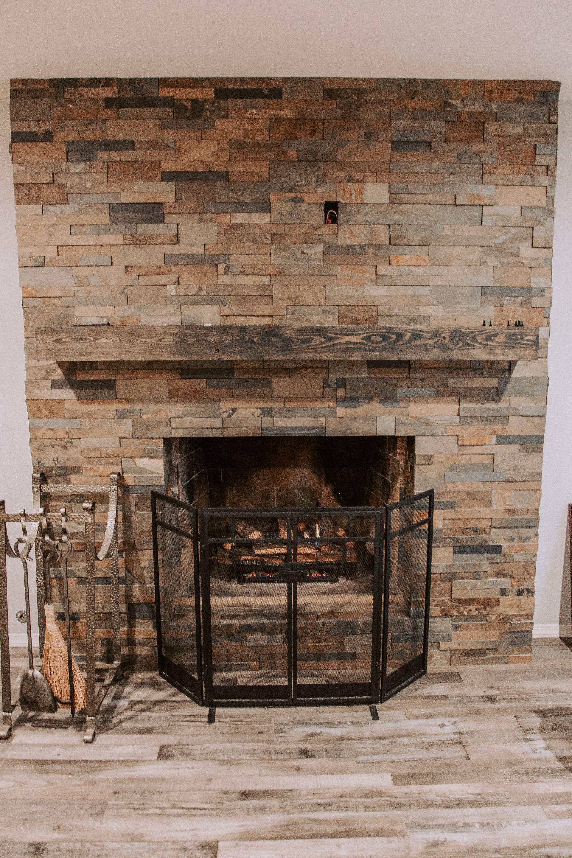 Fireplace with stone facade, wooden mantle, and fire screen. Fire burning inside the hearth.