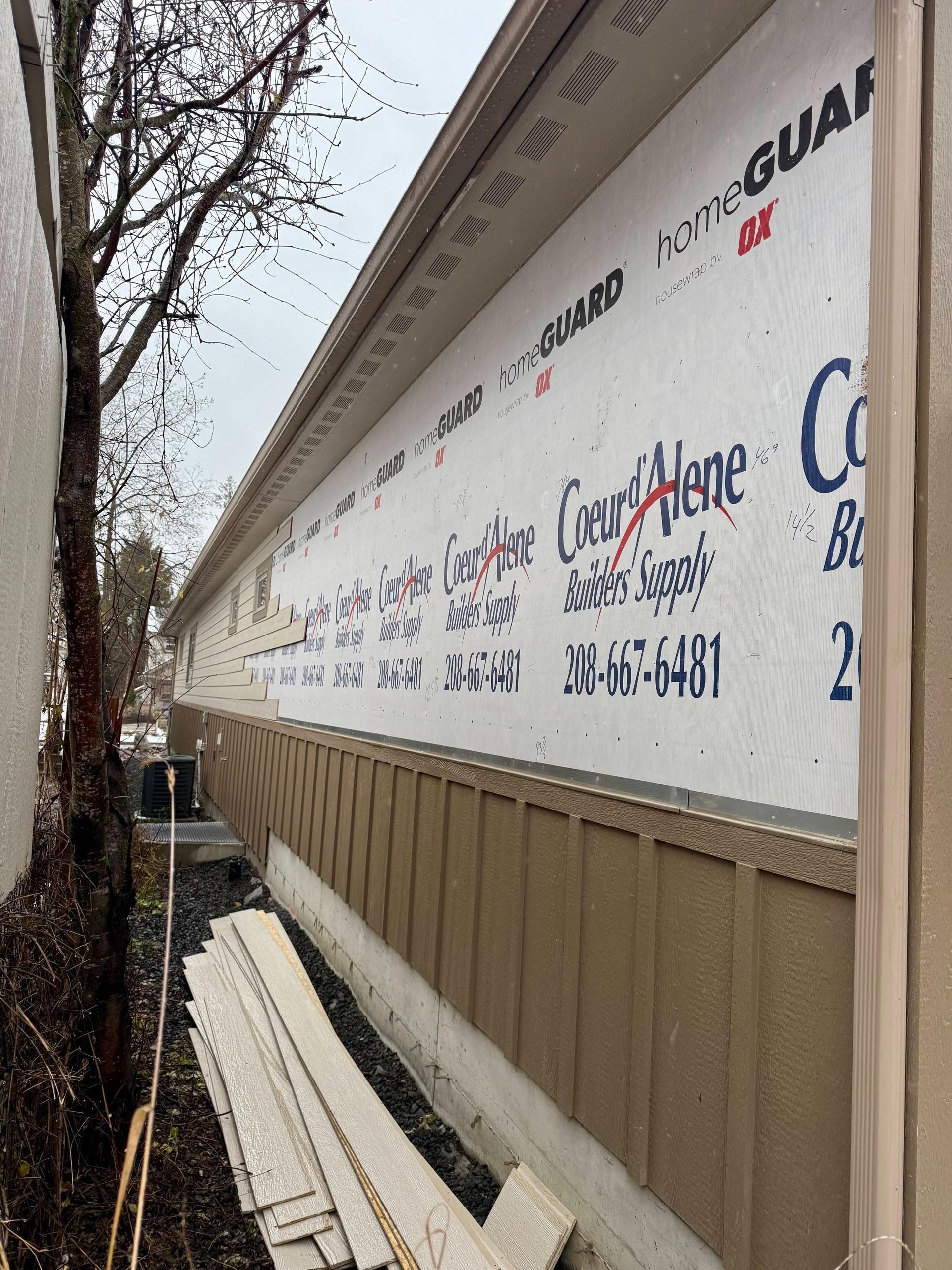 Exterior wall under construction, with beige siding, white house wrap, and exposed soffit.
