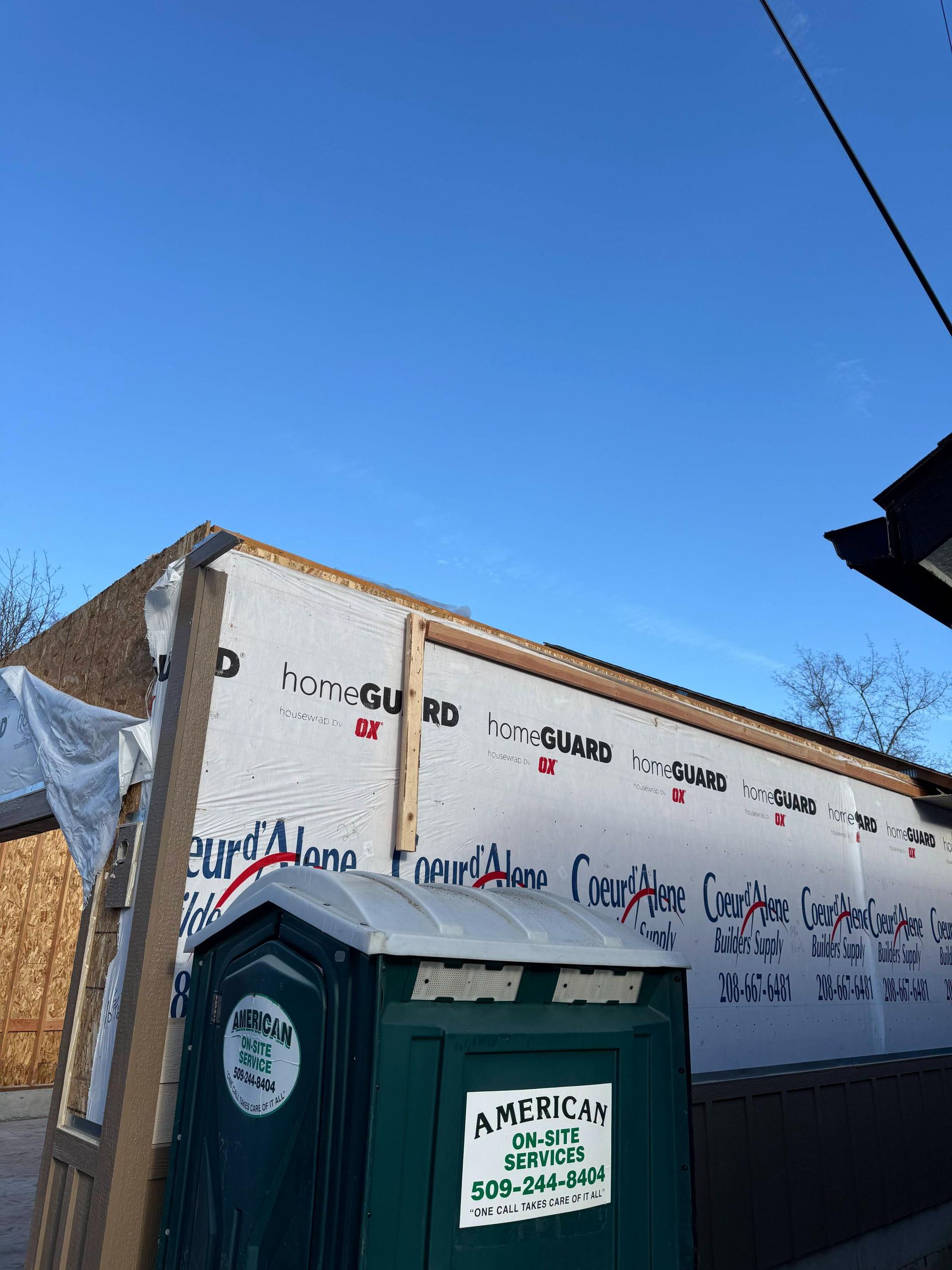 Construction site with a portable toilet and sheathing on a building under a blue sky.
