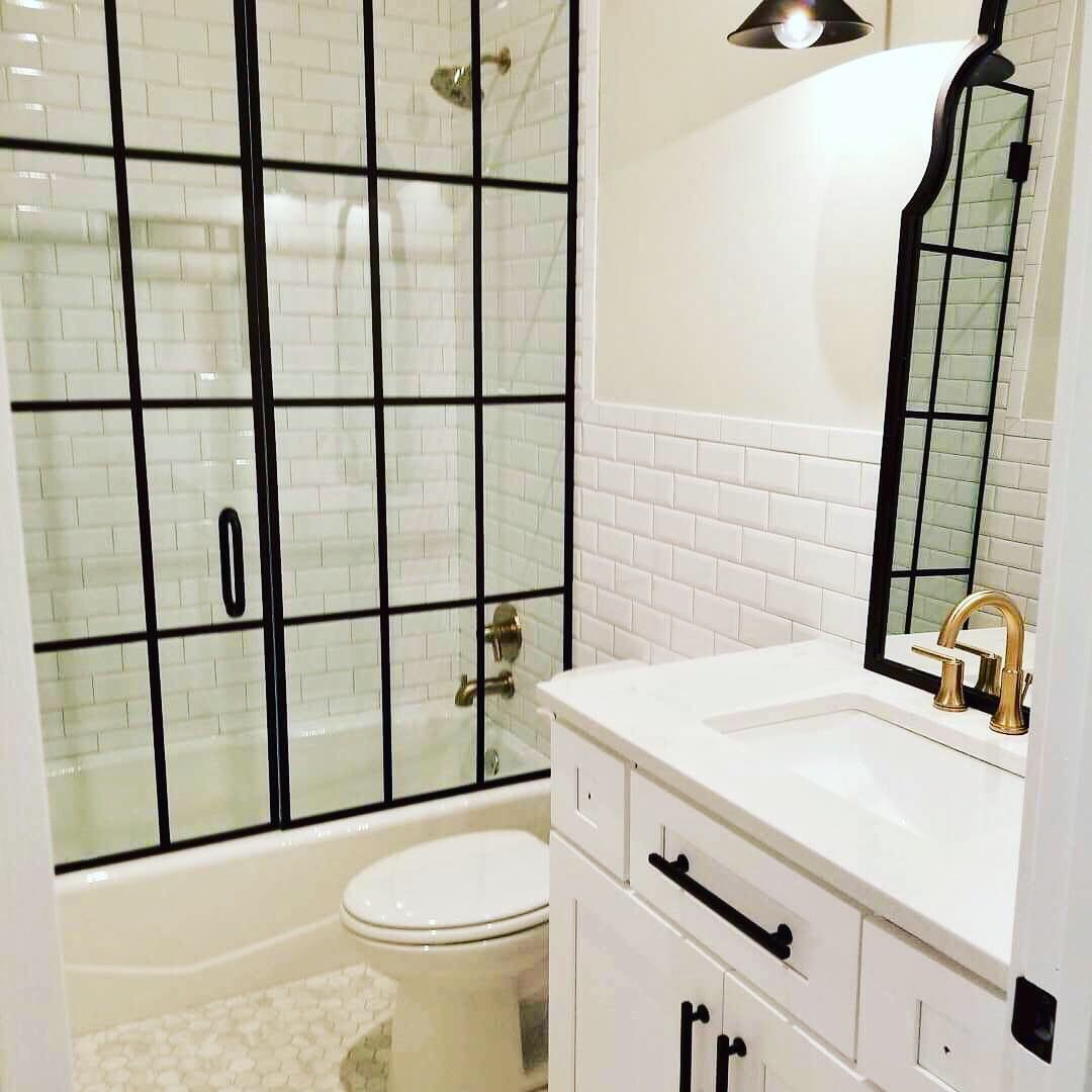 Bathroom with white subway tiles, black framed shower, white vanity, gold fixtures, and toilet.