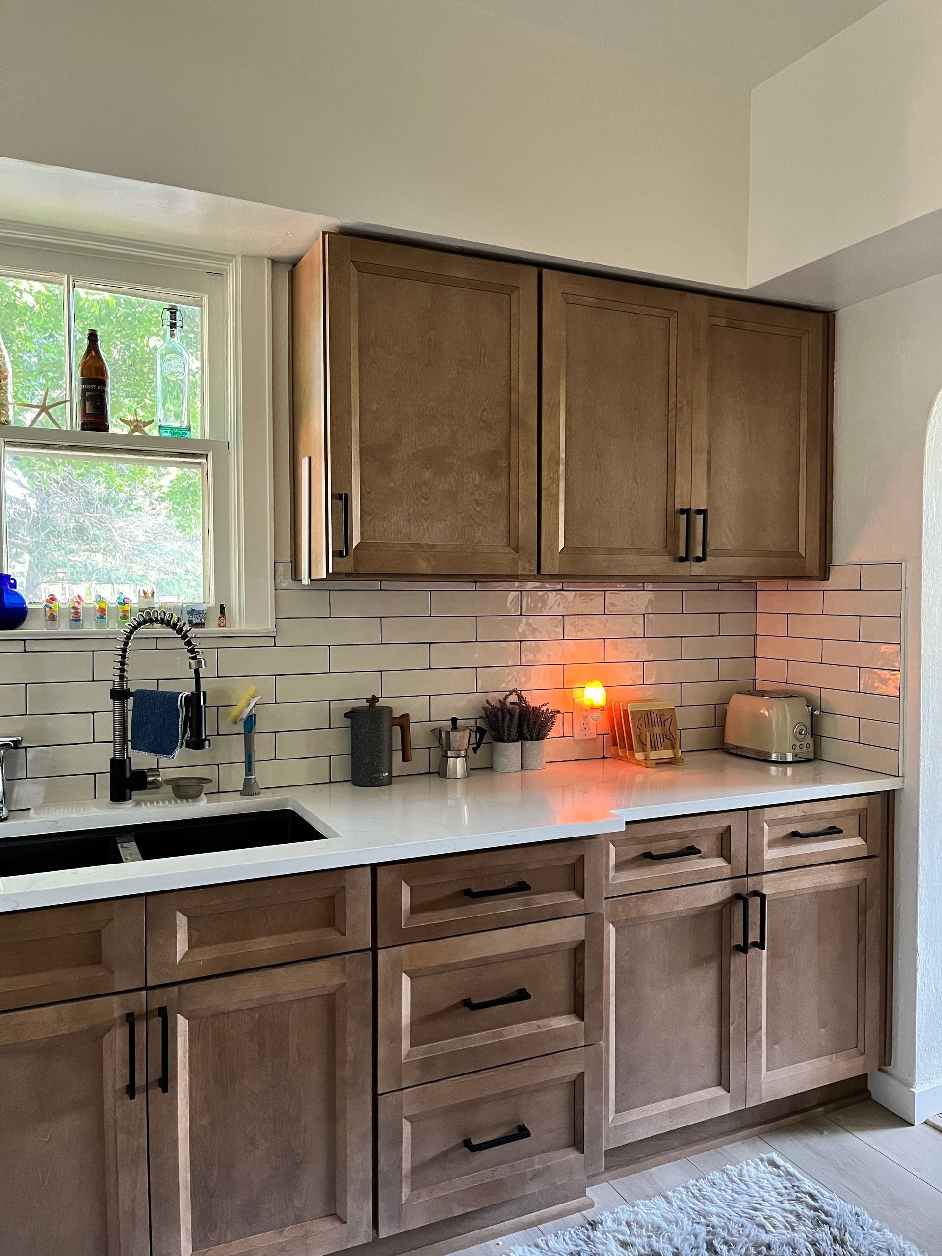 Kitchen with light wood cabinets, subway tile backsplash, and black hardware.