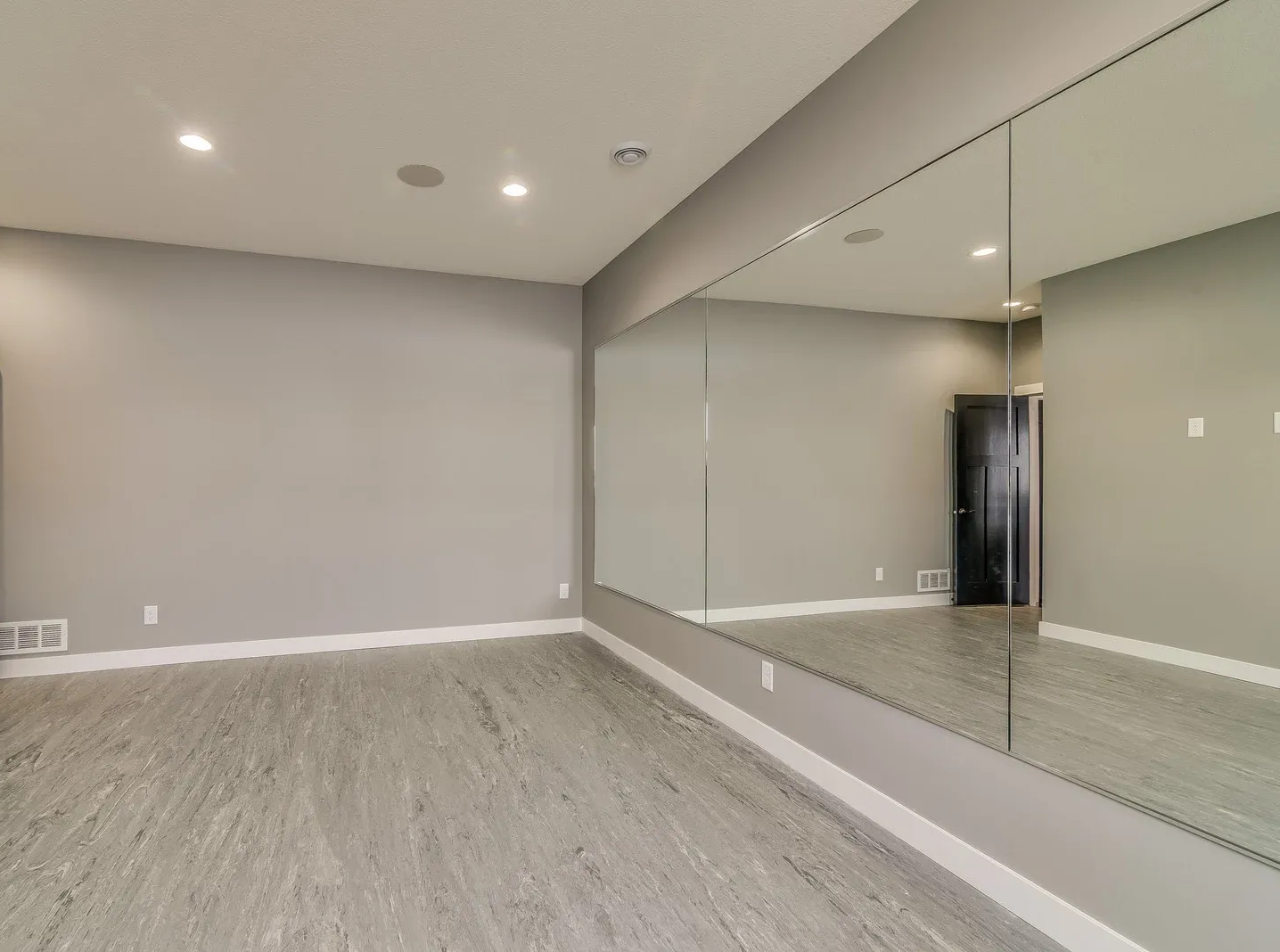 Empty dance studio with gray walls, large mirror, and recessed lighting.