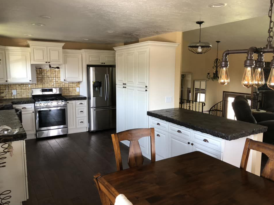 White kitchen with dark wood floor, stainless steel appliances, white cabinets, and a dark island counter.