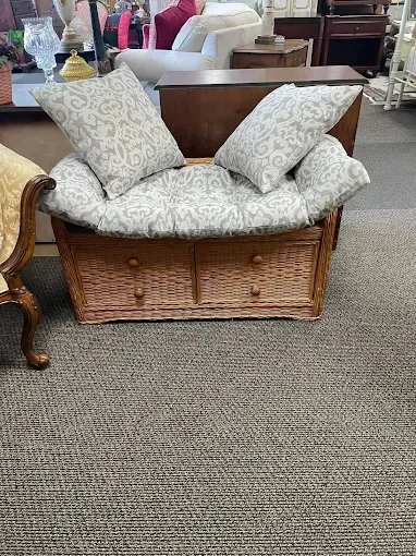 A wicker bench with pillows and drawers in a living room.