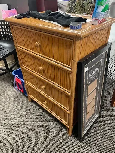 A wicker dresser is sitting on a carpet next to a picture frame.
