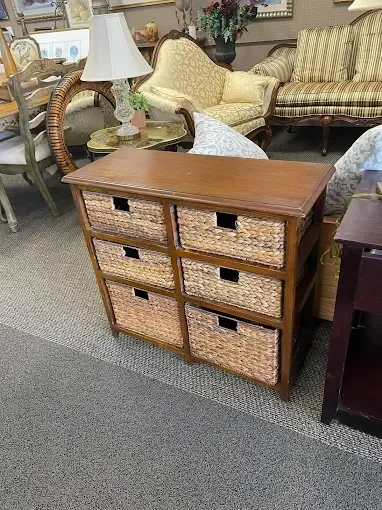 A wooden chest of drawers with wicker baskets in a living room.