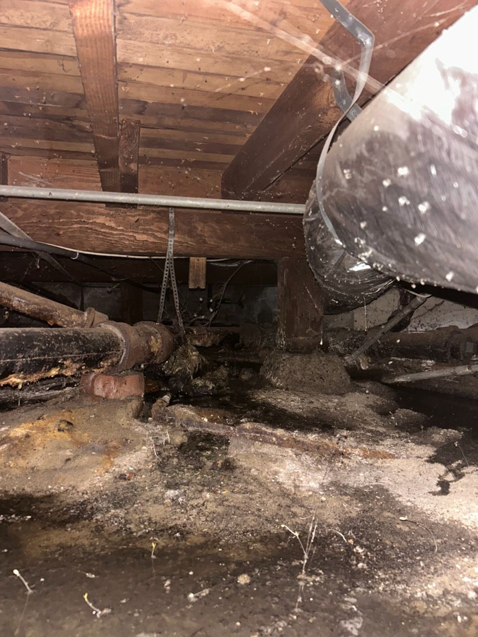 A dirty crawl space with a lot of pipes and wires in Costa Mesa.