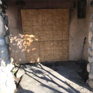 A door with a piece of plywood on it is sitting next to a stone wall in Huntington Beach.
