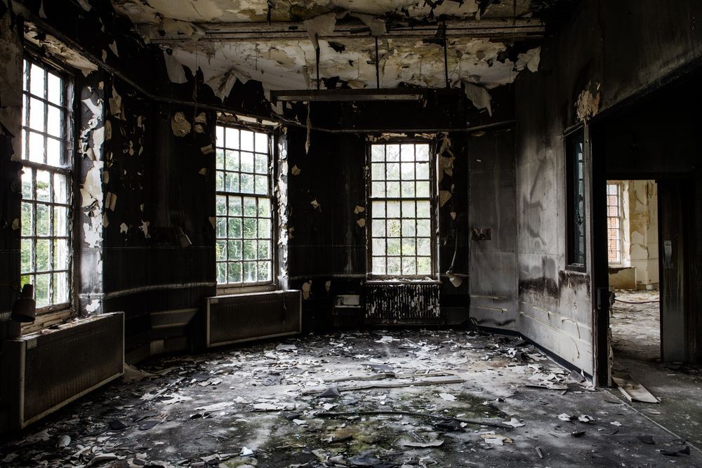 An abandoned room with a lot of windows and a lot of trash on the floor.