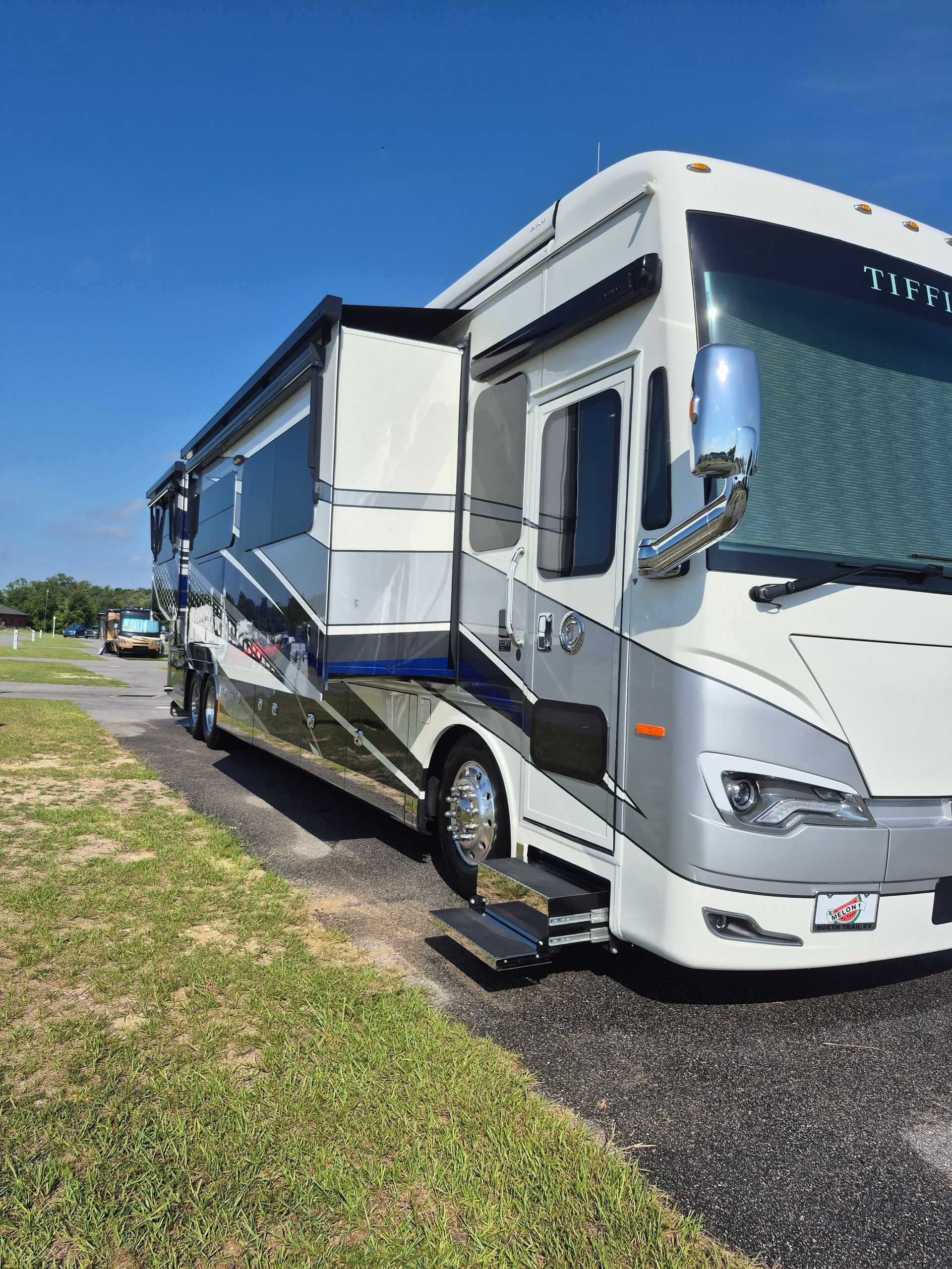 A large white and silver rv is parked in a grassy field.