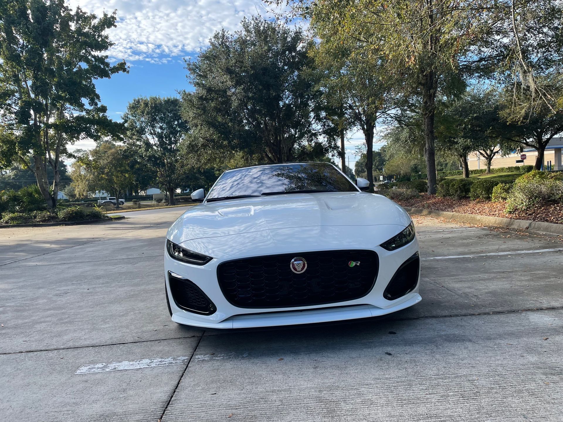 A white jaguar f type convertible is parked in a parking lot.