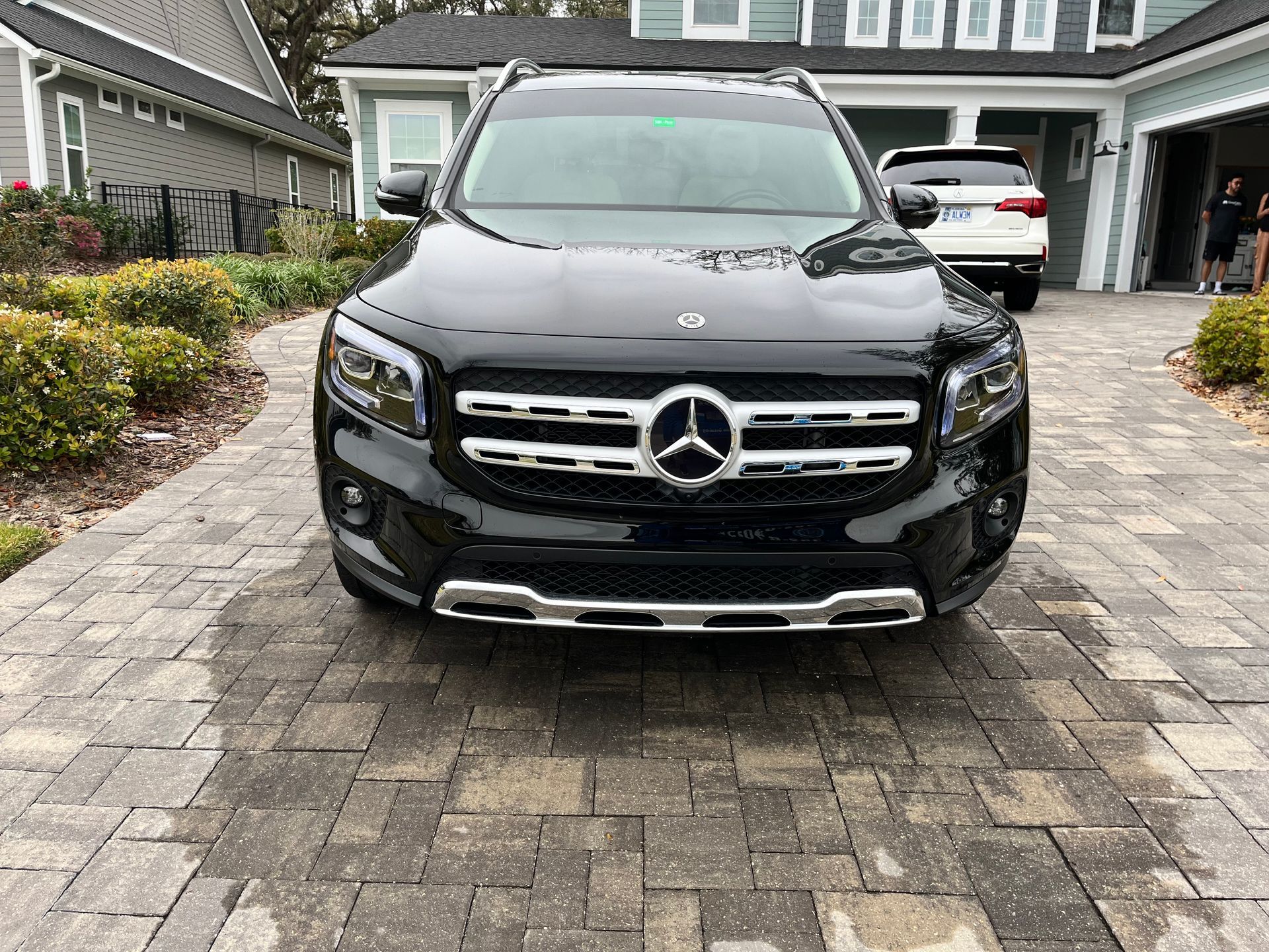 A black mercedes benz glb is parked in front of a house on a brick driveway.