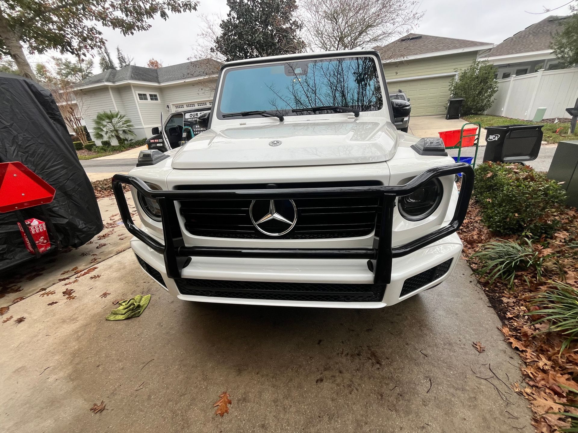 A white mercedes benz g63 with a black bumper is parked in a driveway.