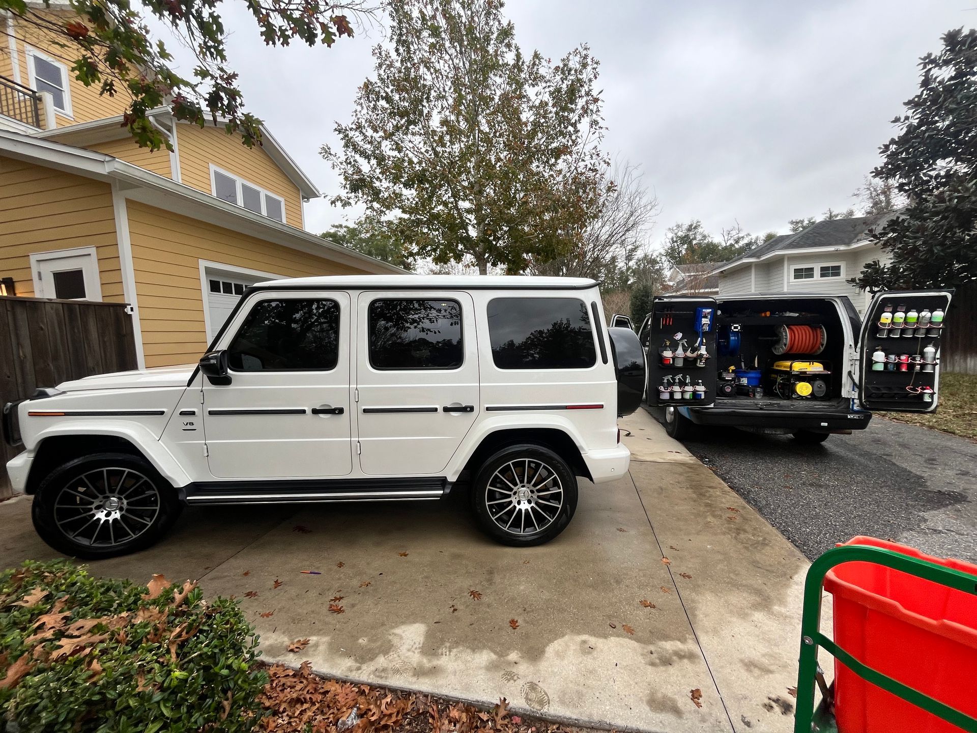 A white suv is parked in front of a yellow house.
