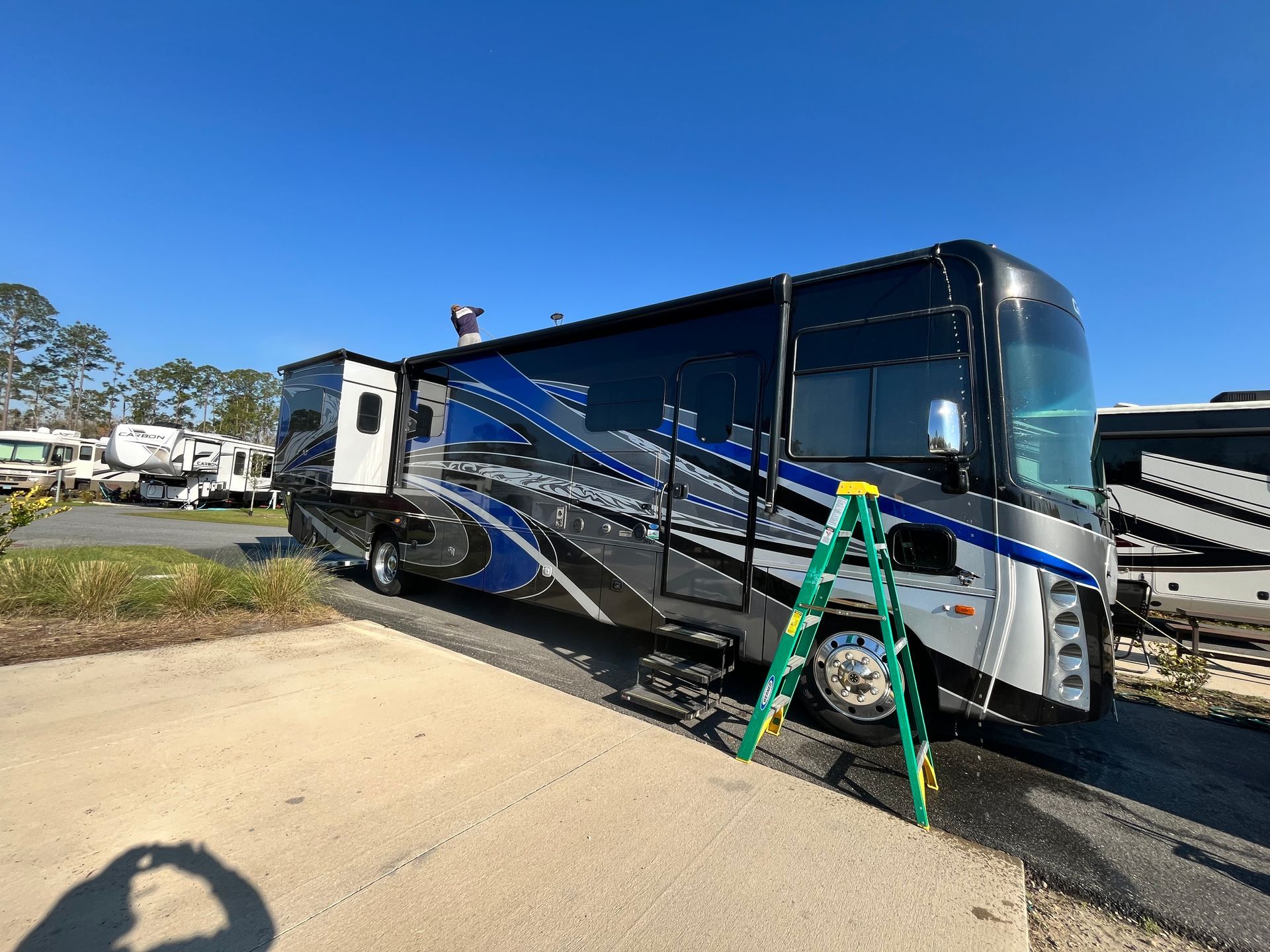 A large rv is parked on the side of the road next to a ladder.