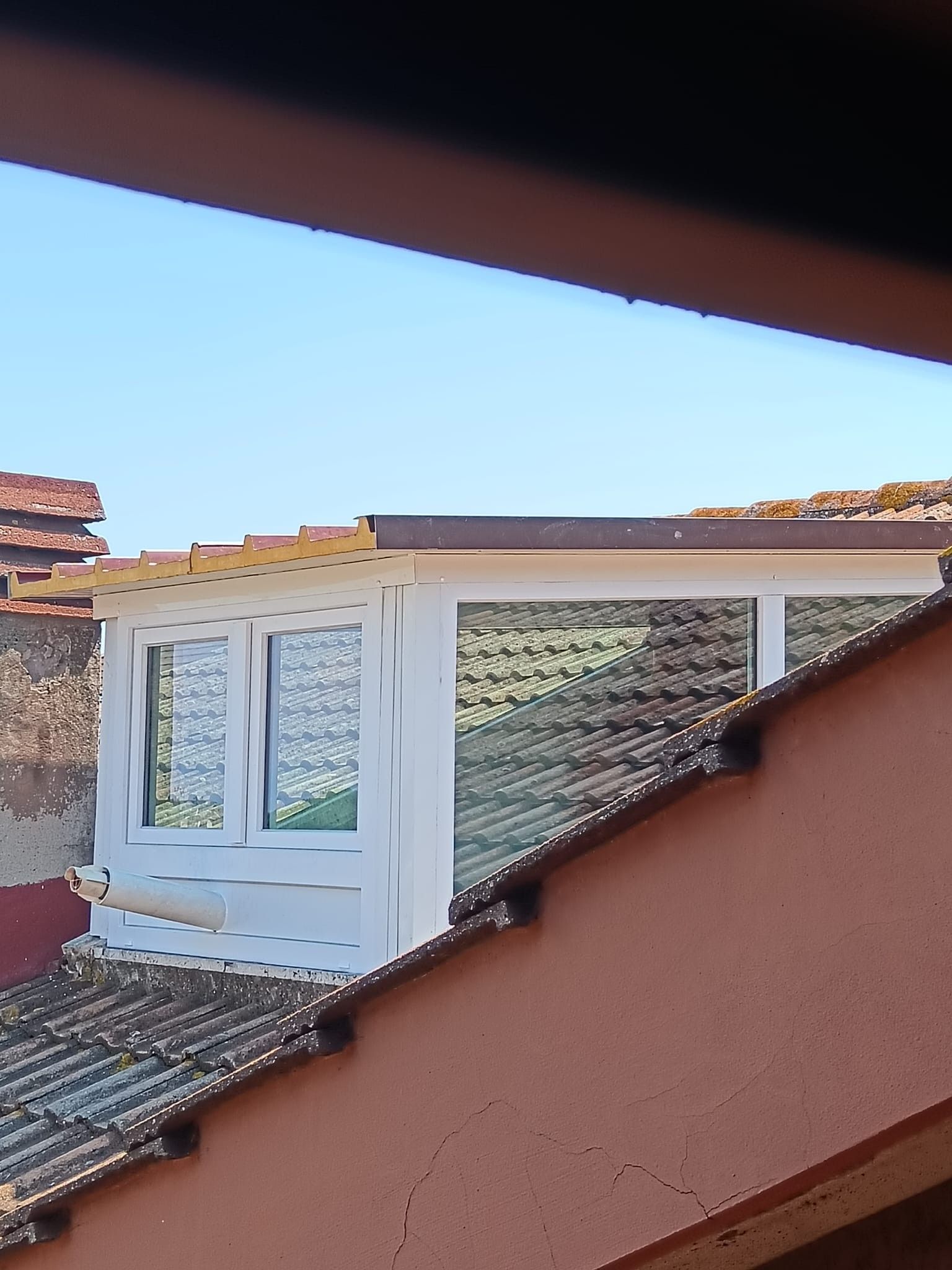 Finestra a abbaino con cornice bianca su un tetto di tegole sotto un cielo azzurro.