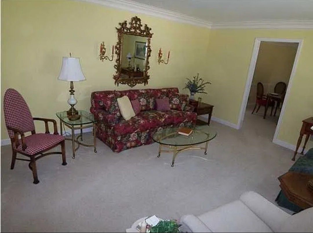 Living room with floral sofa, ornate mirror, and red and cream chair. Yellow walls, neutral carpet.