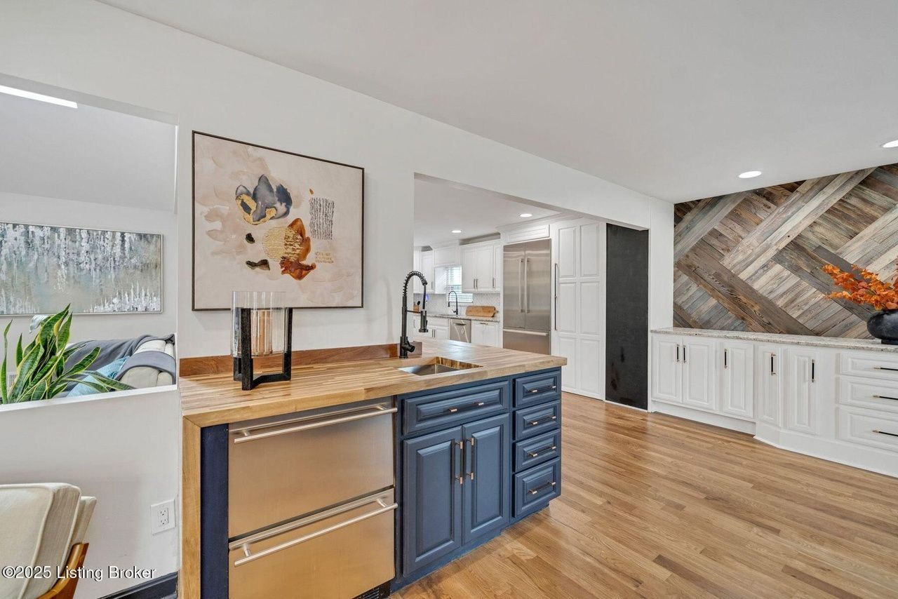 Kitchen island with a sink and mini-fridge, navy cabinets, wooden countertop, hardwood floors, and accent wall.