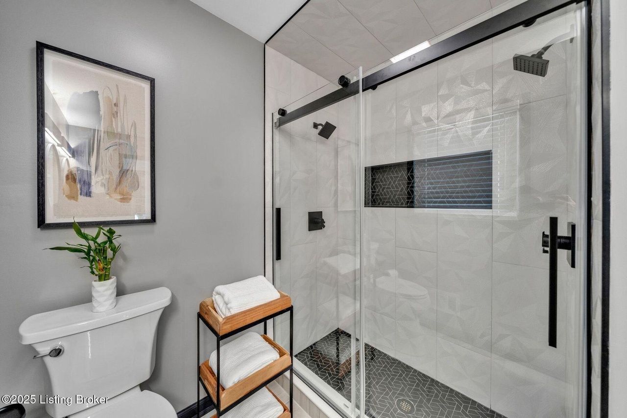 Modern bathroom with gray walls, glass shower, black fixtures, and artwork.