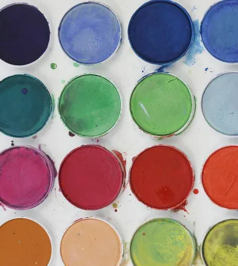 Watercolor paint palette with circular wells filled with various bright colors.