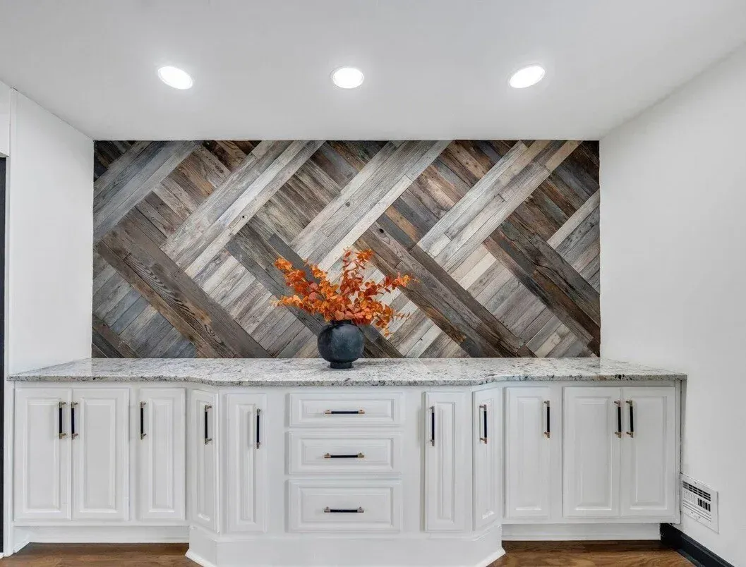 White cabinets with gray countertop and chevron wood backsplash, orange flowers in vase.