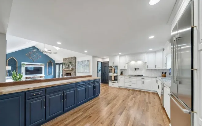 Open-concept kitchen with navy island and white cabinets, wood floors, stainless steel appliances, and blue living room.