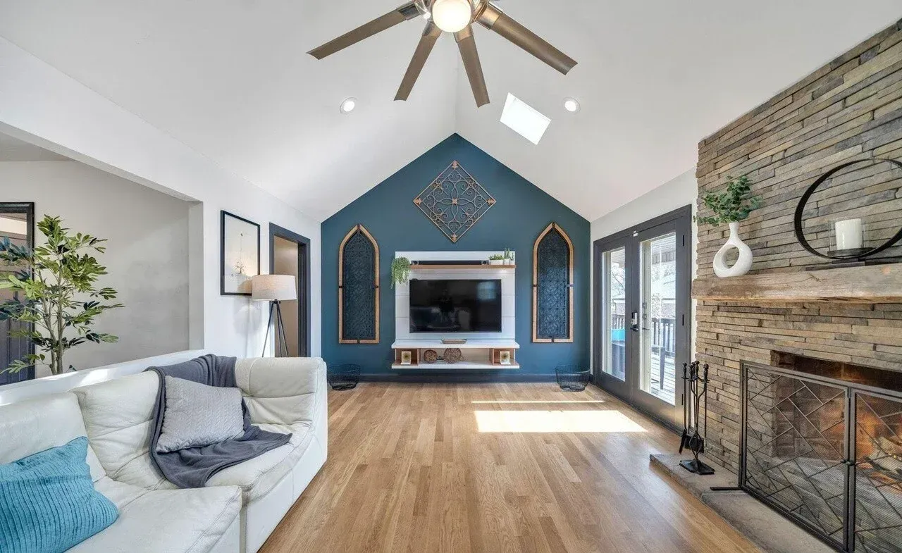 Living room with vaulted ceiling, hardwood floor, white sofa, fireplace, and blue accent wall with TV.