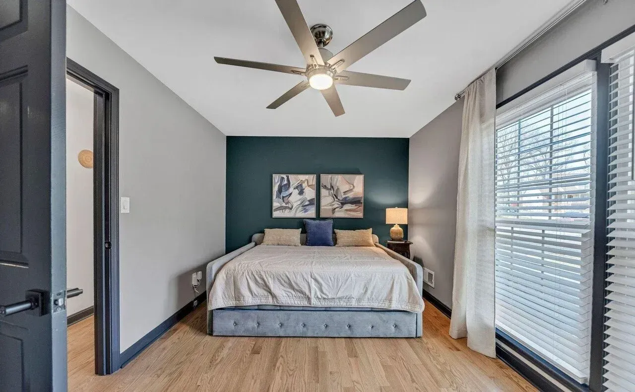 Bedroom with teal accent wall, bed, window, and ceiling fan.