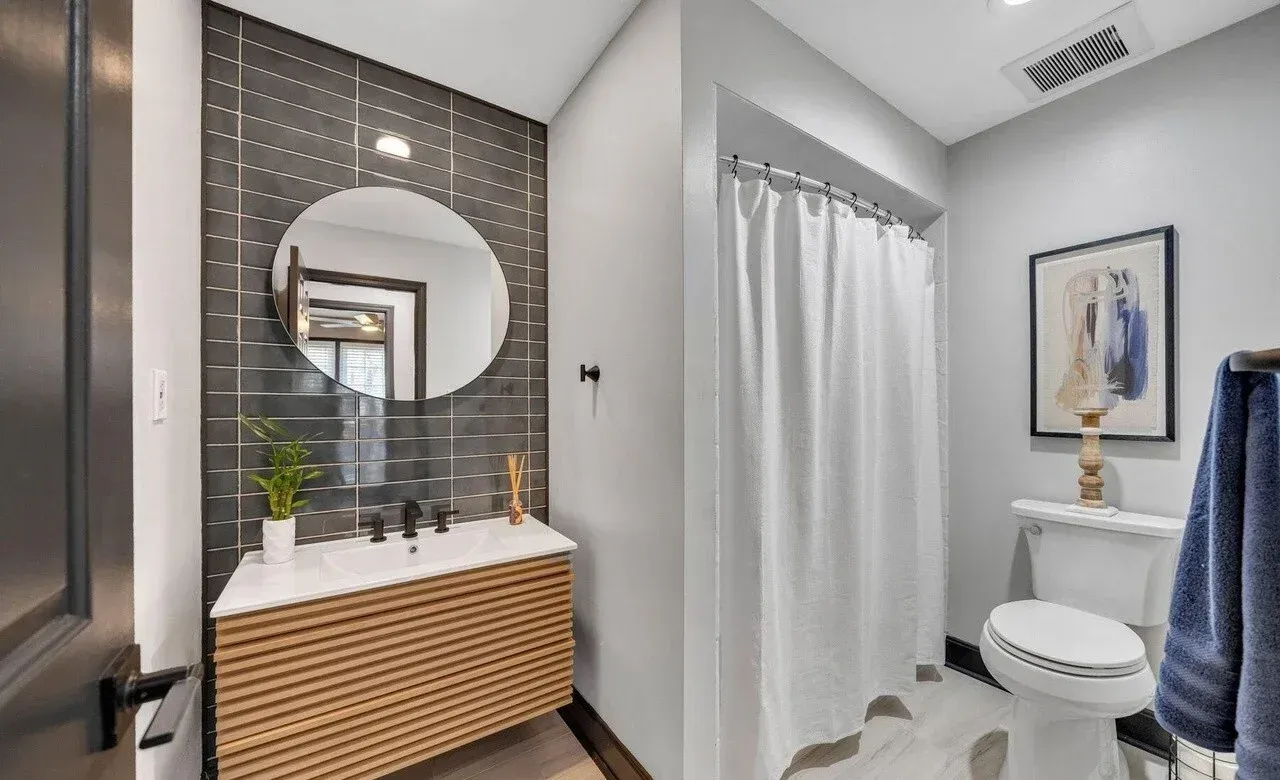 Modern bathroom with a wooden vanity, round mirror, and white shower curtain.