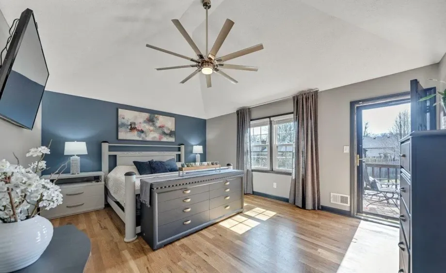 Bedroom with wood floors, blue accent wall, bed, dresser, and access to a patio.