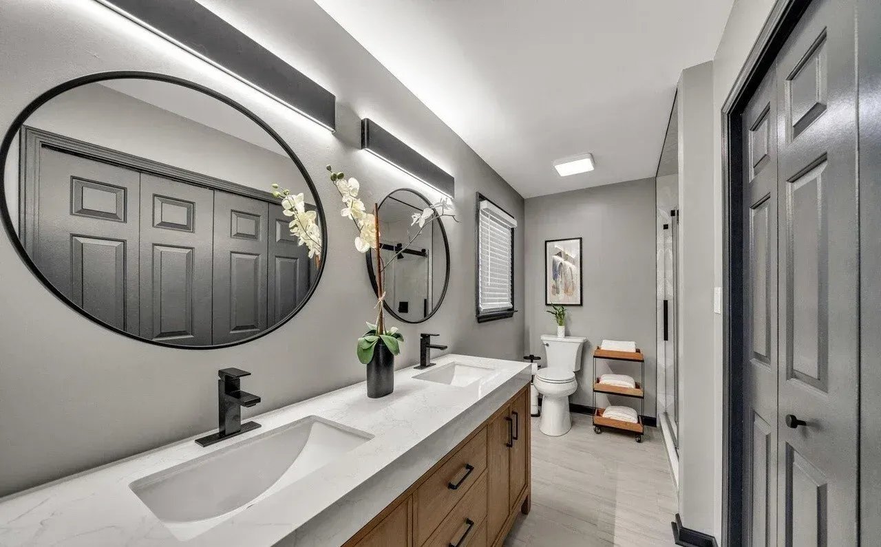Modern bathroom with double vanity, round mirrors, and gray walls.