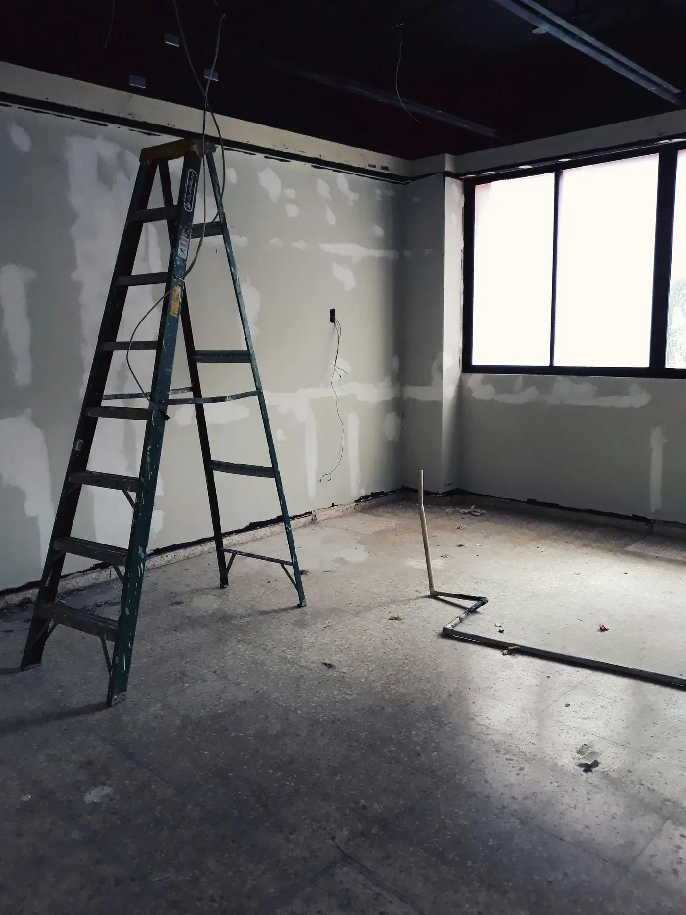A ladder in an unfinished room with bare walls and a window. Construction is underway.