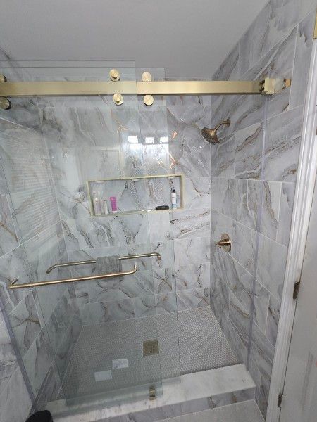 Gold-framed, marble-tiled shower with glass door, showerhead, and shelf. Gold fixtures.