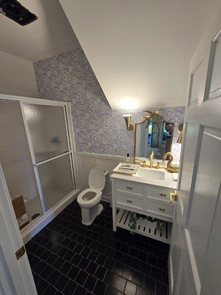 Bathroom with black tiled floor, white vanity, blue and white wallpaper, and a glass shower.