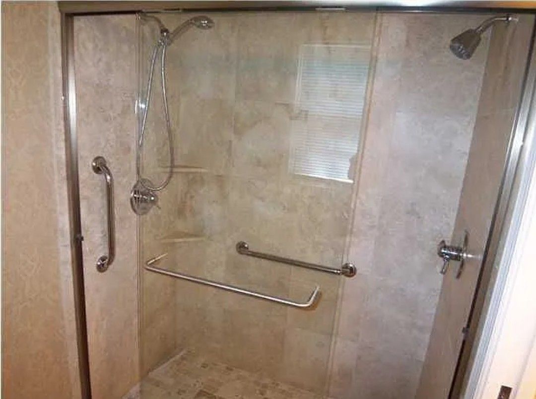 Shower with beige tile, glass doors, and grab bars for accessibility.