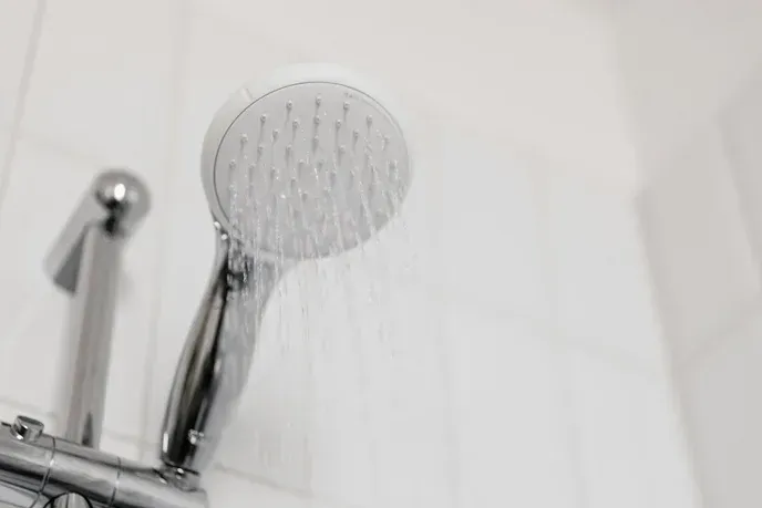 Showerhead spraying water, close-up, chrome fixtures, white tiled wall.