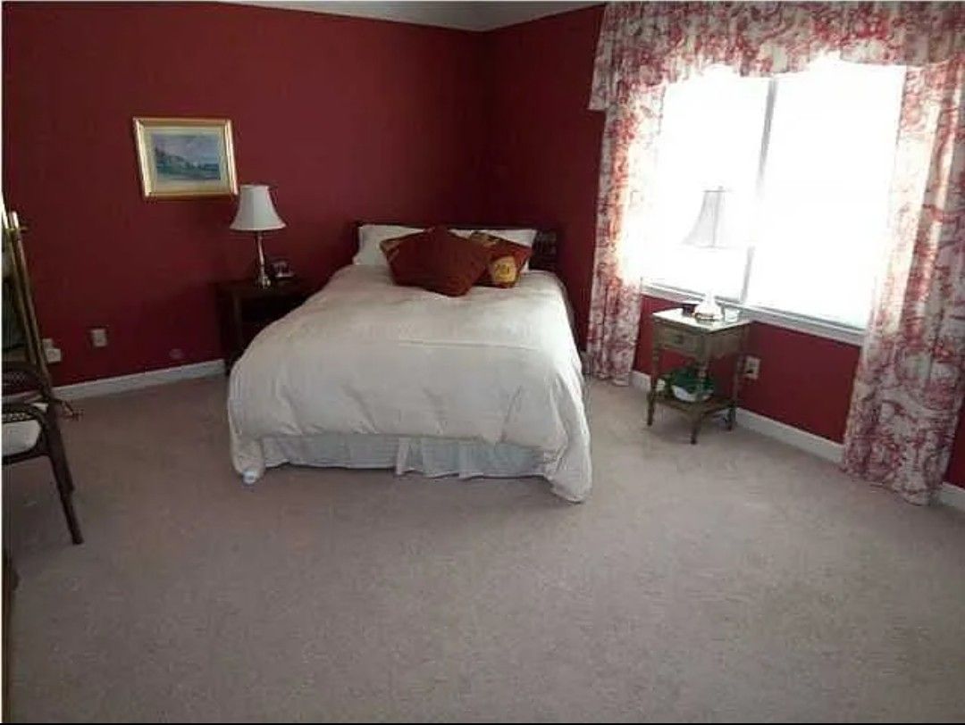 Bedroom with red walls, white bed, floral curtains, and two nightstands.