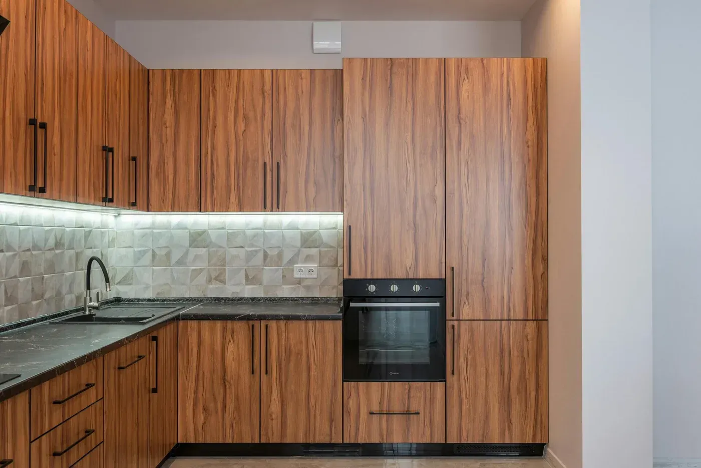 L-shaped kitchen with wood grain cabinets, black countertops, and built-in oven.