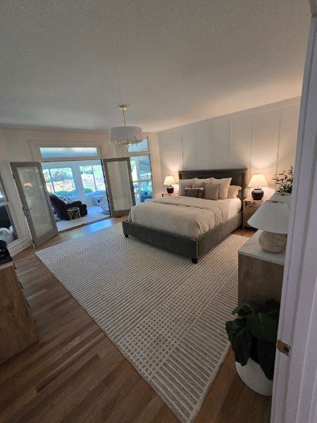 Spacious bedroom with a gray bed, large rug, and French doors leading to an outdoor sitting area.