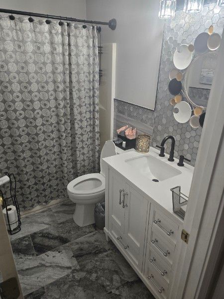 Bathroom with white vanity, gray patterned tile, toilet, shower curtain, and decorative mirror.