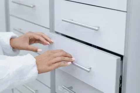 Hands opening a white drawer in a cabinet, likely in a medical or laboratory setting.