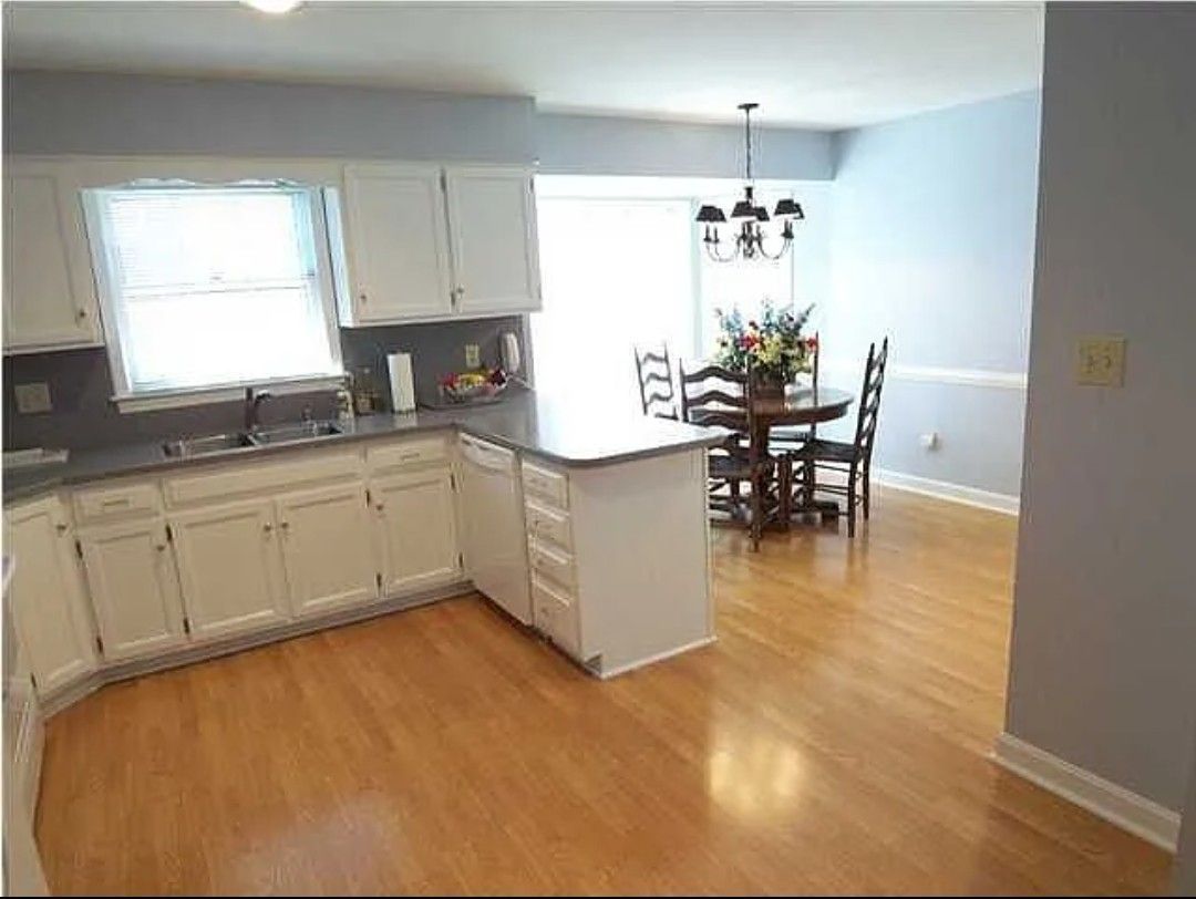Kitchen with white cabinets, island, dining area with wood table and chairs, hardwood floors.