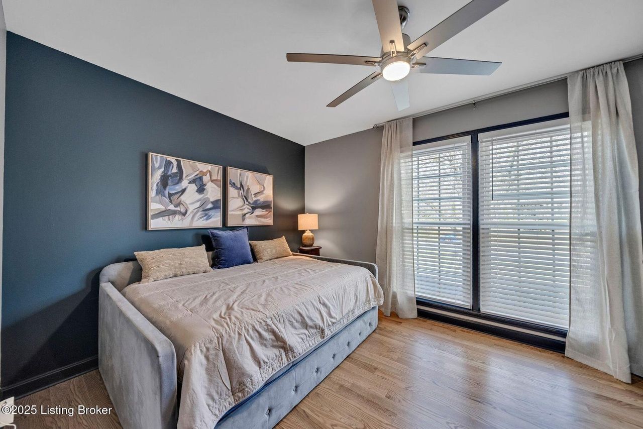 Bedroom with daybed, dark blue accent wall, and large window with white blinds.