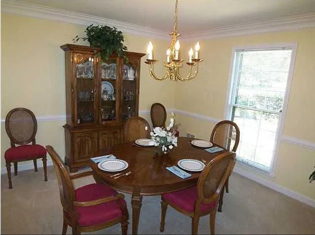 Dining room with a round table, six chairs, a cabinet, and a chandelier. Yellow walls, white trim.