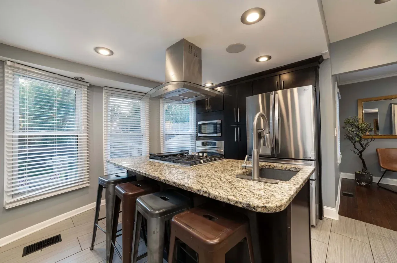 Kitchen island with stainless steel appliances, granite countertop, bar stools, and windows.