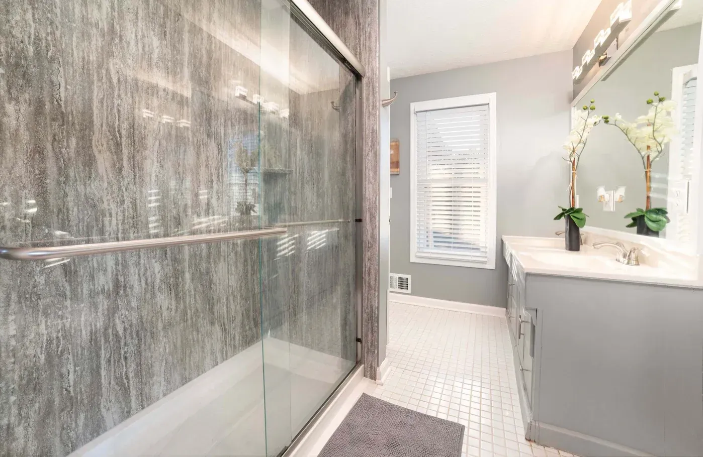 Modern bathroom with gray shower, vanity, window, and white tile floor.