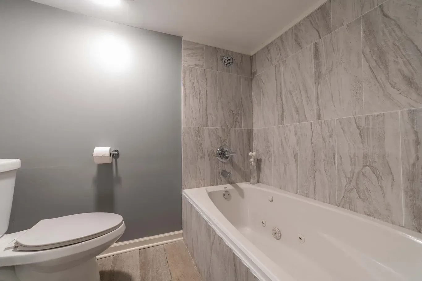 Bathroom with toilet, white bathtub, and gray tiled walls.
