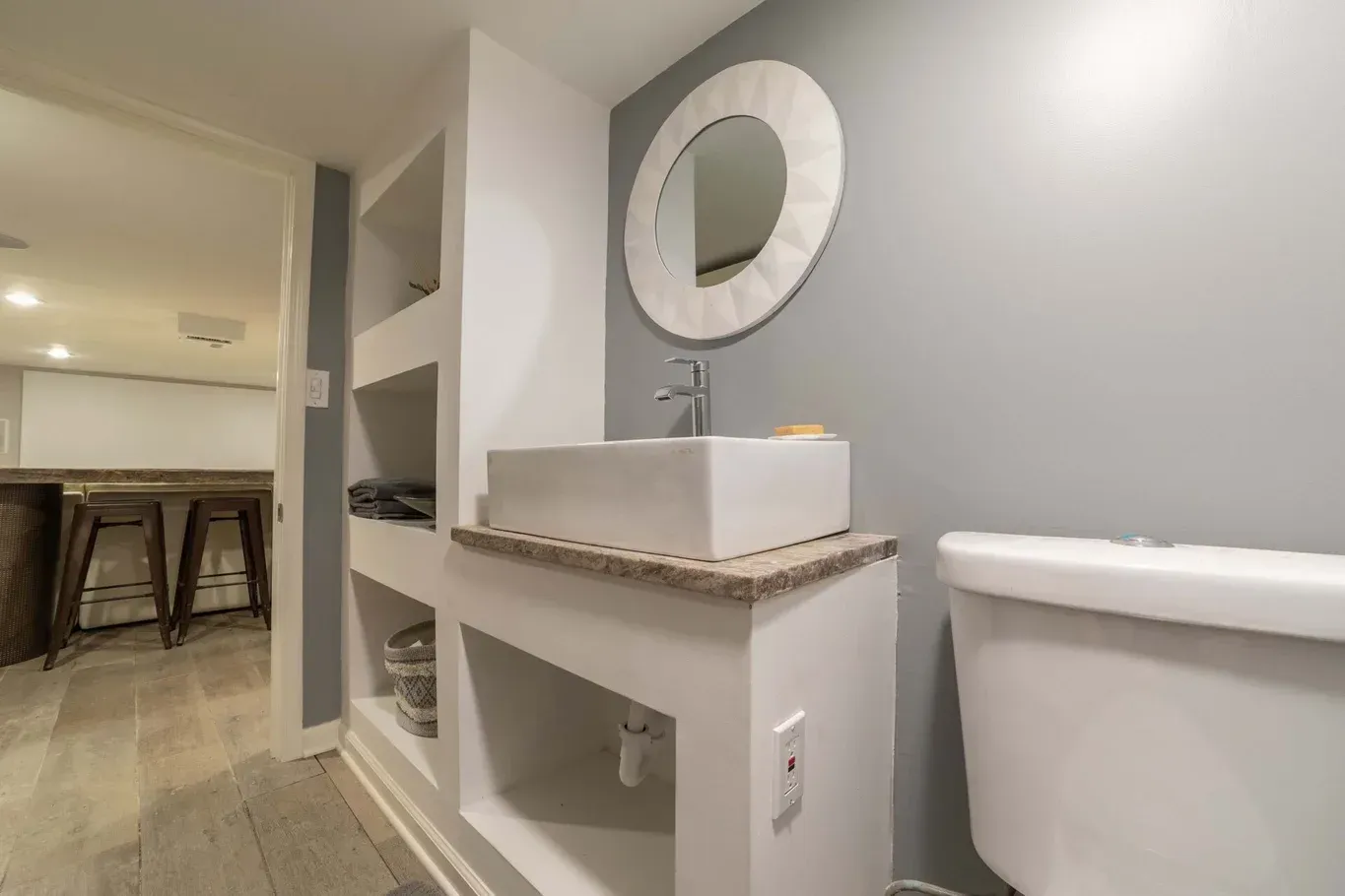 Bathroom with a gray wall, white sink, and toilet. Built-in shelves and a mirror.